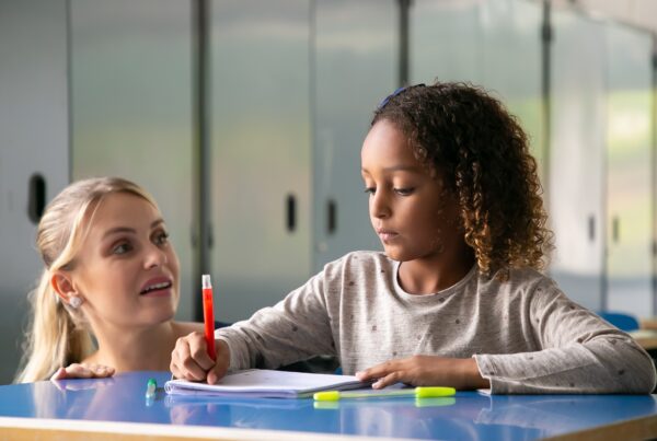positive female school teacher helping curly haired girl her task 1
